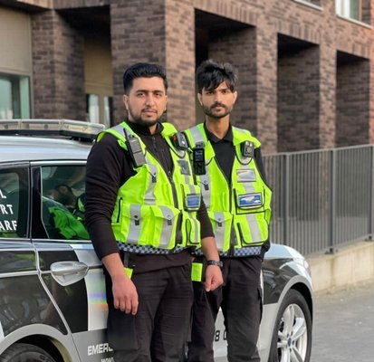 Two security personnel in yellow vests stand by a marked vehicle labeled 'Royal Albert Wharf'. They look alert and professional, conveying readiness.